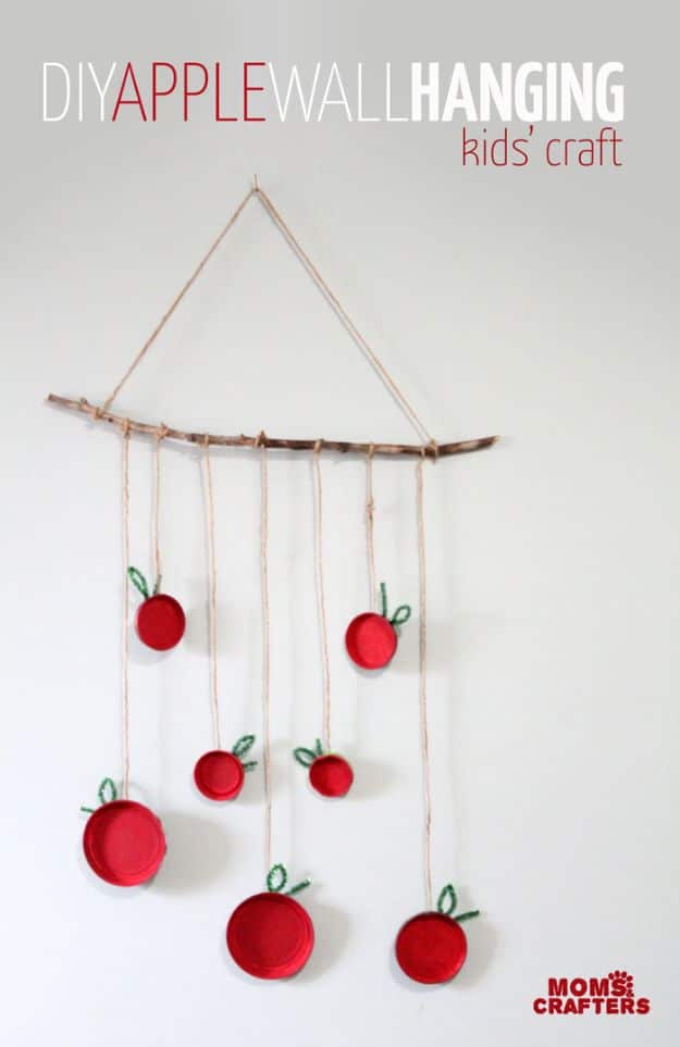 Apple Wall Hanging Fall Craft for Kids Pin graphic, DIY Apple Wall Hanging Kids Craft, red painted jar lids with pipe cleaner leaves hung from a stick