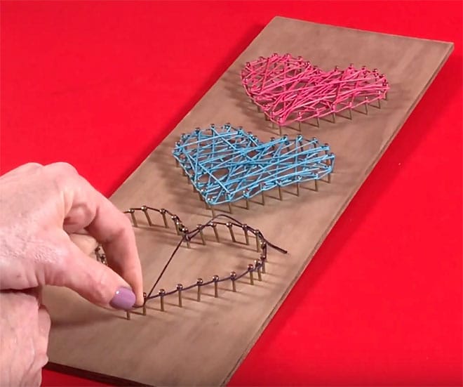 Colorful string art on a wooden board forming a heart shape – trendy handmade craft that sells well during the holidays or for dorm room decor