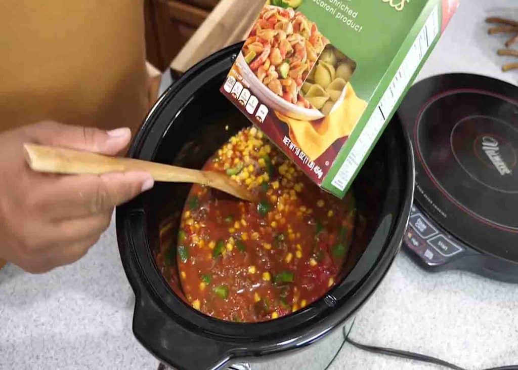 Adding the pasta shell into the crock-pot with sauce