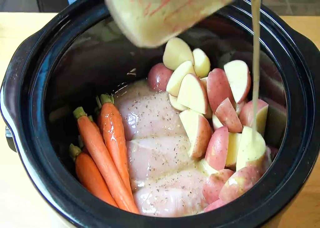 Pouring the marinade into the slow cooker where the chicken, potatoes, and carrots are