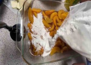 Dumping all the peach cobbler cake ingredients in the baking dish