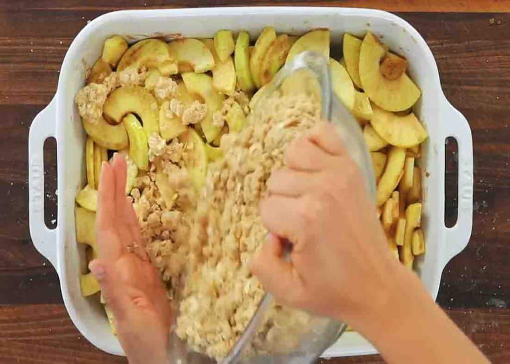 Adding the topping over the apples for apple crisp recipe