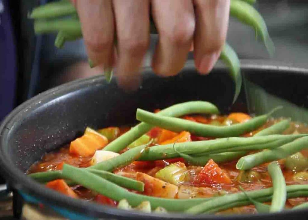 Adding the green beans on top of the Italian chicken stew