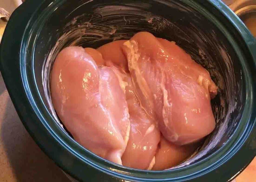 Adding the chicken breasts to the crock pot for the cheesy bacon ranch chicken recipe