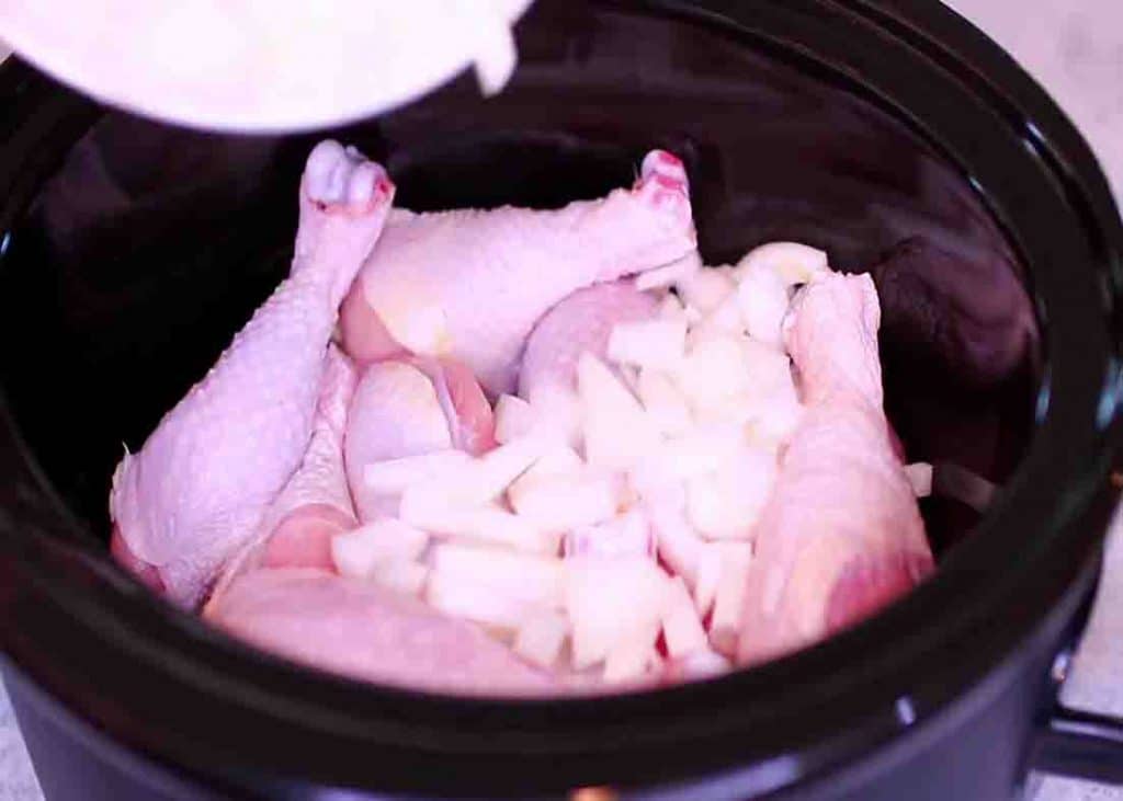 Adding the diced onion to the slow cooker with the chicken drumsticks