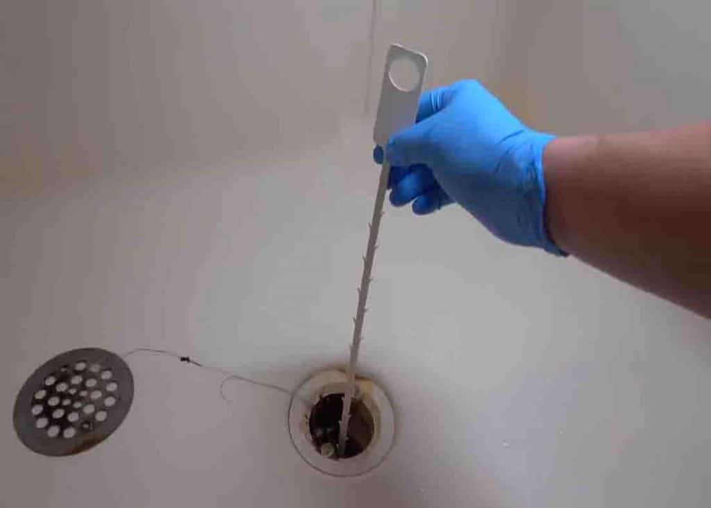 Clearing out the shower drain clog with a drain clearing tool