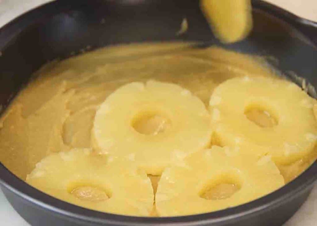 Adding the pineapple slices to the bottom of the cake pan