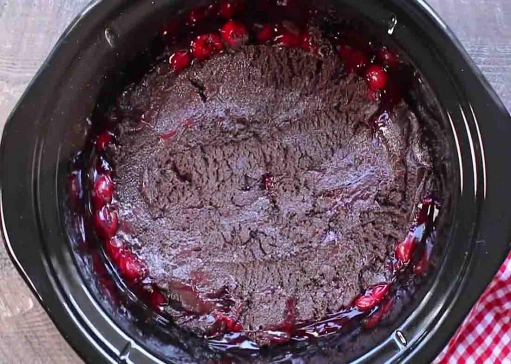 Adding the cake batter over the cherries on the slow cooker