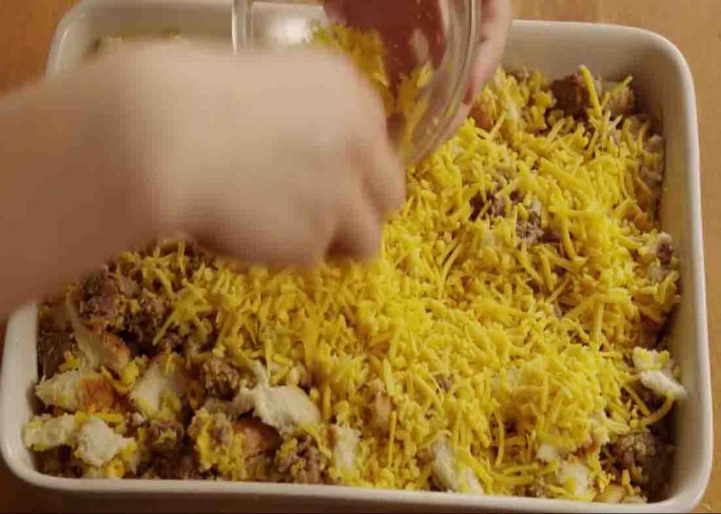 Topping the egg casserole with shredded cheddar cheese