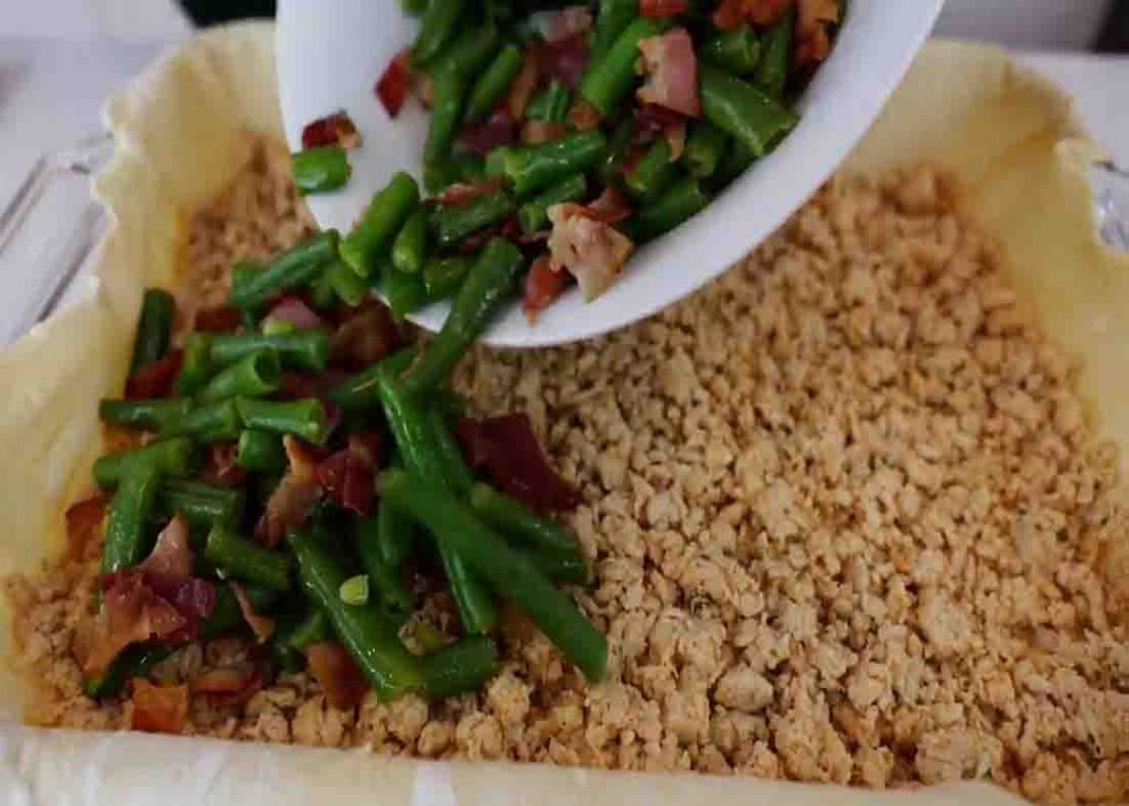 Adding the green beans and bacon to the casserole dish