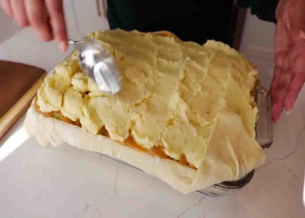 Spreading the mashed potatoes on top of the holiday casserole