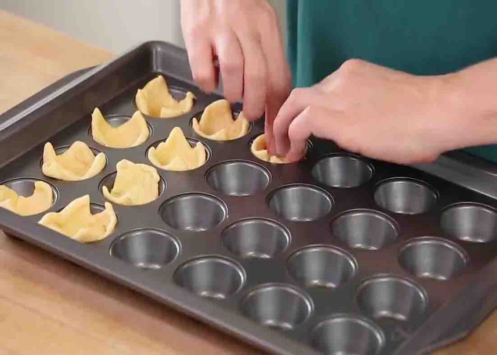 Placing the cranberry brie bites dough on each muffin tin