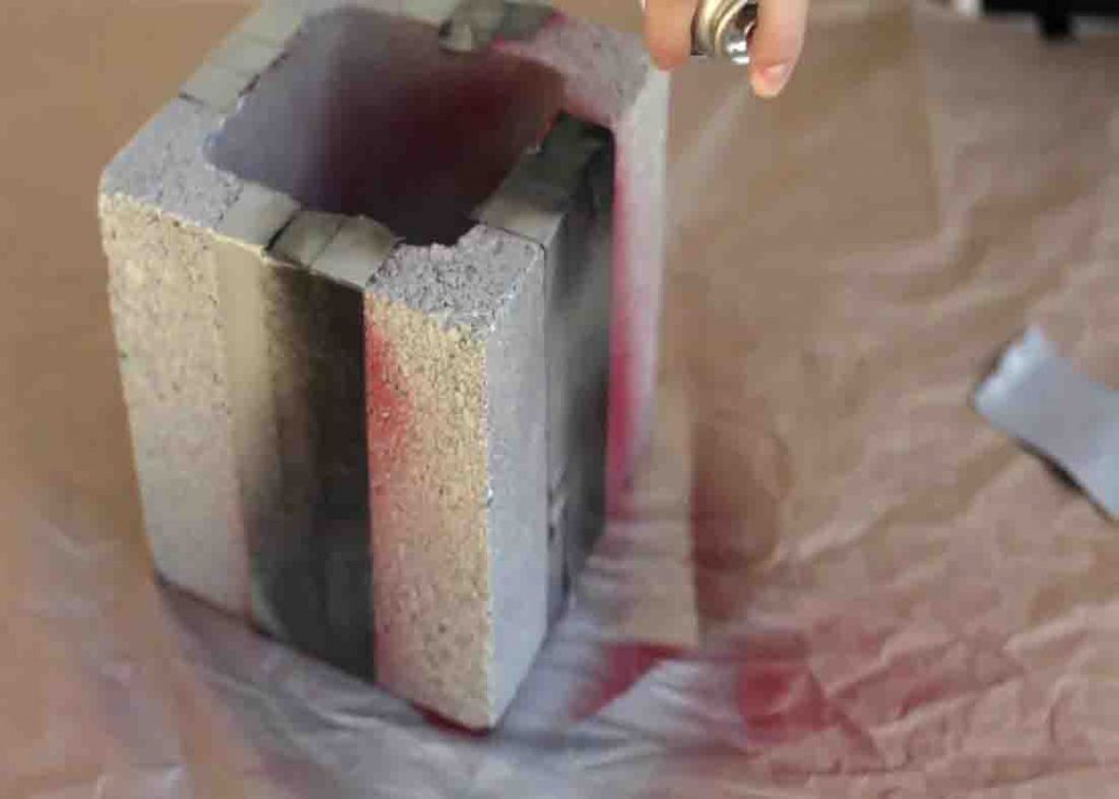 Spraying the cinder block with silver paint for the DIY present decor