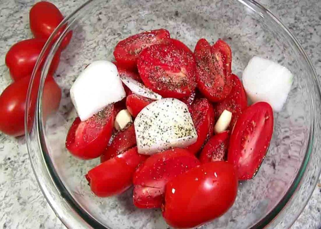 Seasoning the tomatoes and onion before roasting them