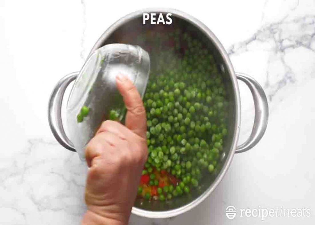 Adding the frozen peas to the smoked sausage and rice dish