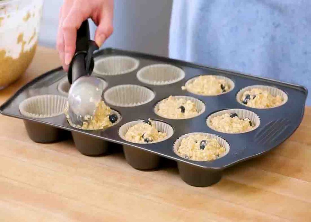Scooping the blueberry oatmeal muffin mixture to the muffin tin