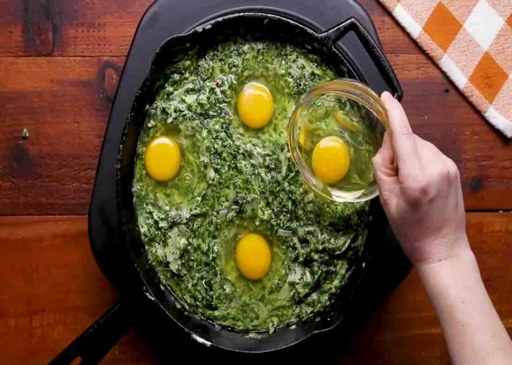 Placing the raw egg on the spinach skillet
