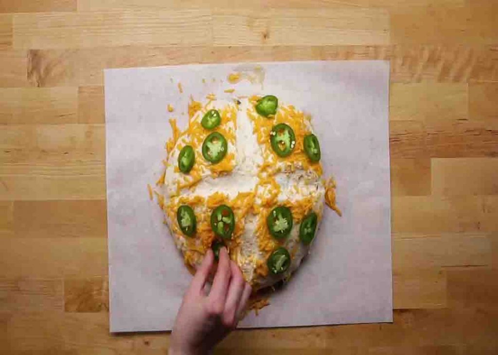 Putting more jalapeno and cheddar cheese on the bread dough