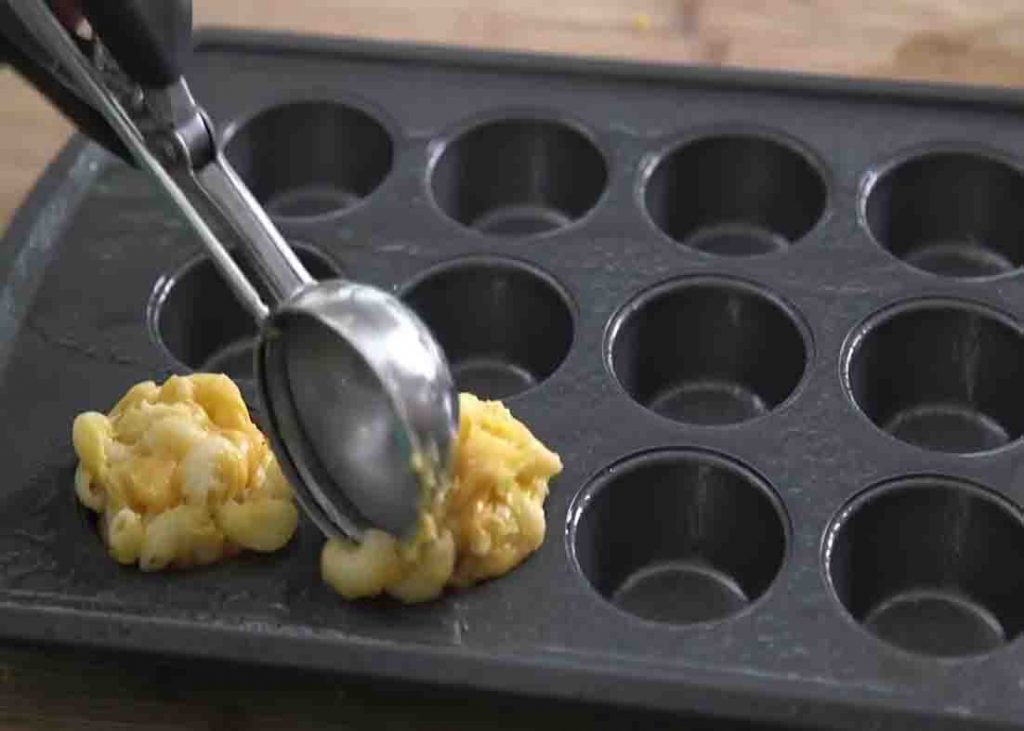 Scooping the mac and cheese into the muffin tins