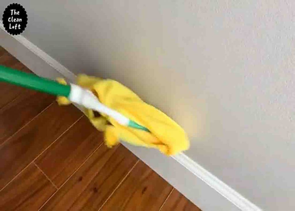 Cleaning the baseboards with wet towel attached to a broom