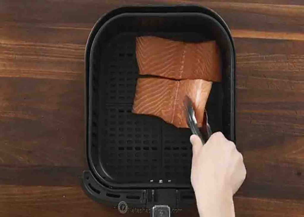 Placing the salmon filets in single layer at the bottom of the air fryer basket