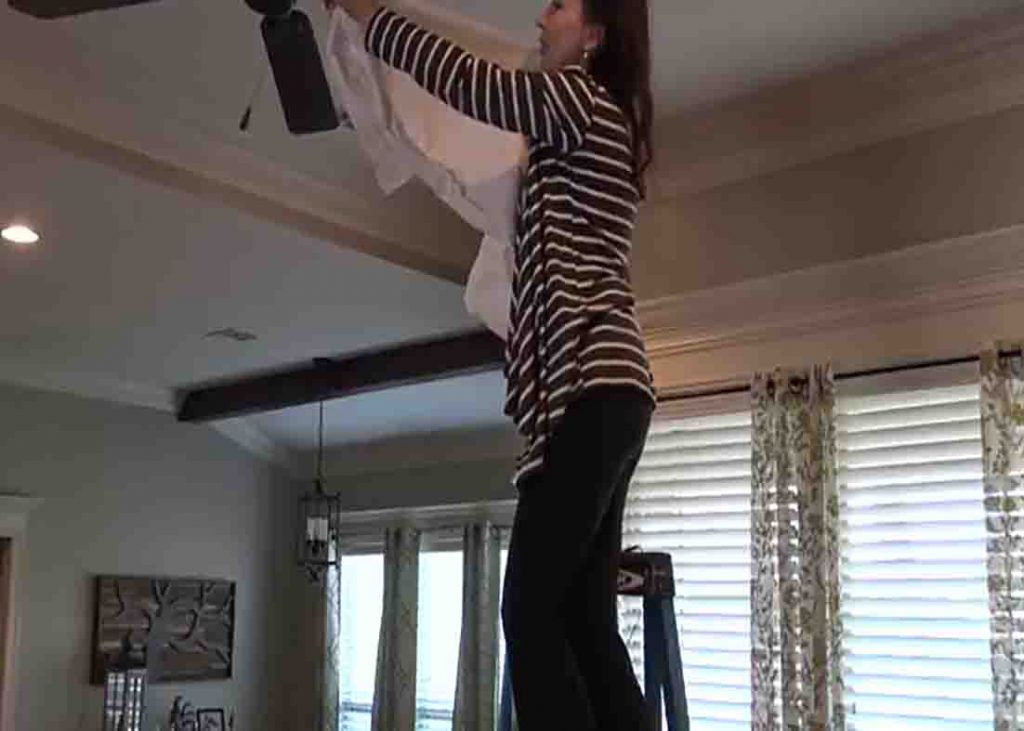 Cleaning the dirty ceiling fan with an old pillowcase
