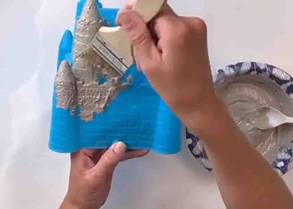 Applying the gray paint to the plastic sandcastle to make the wind chime