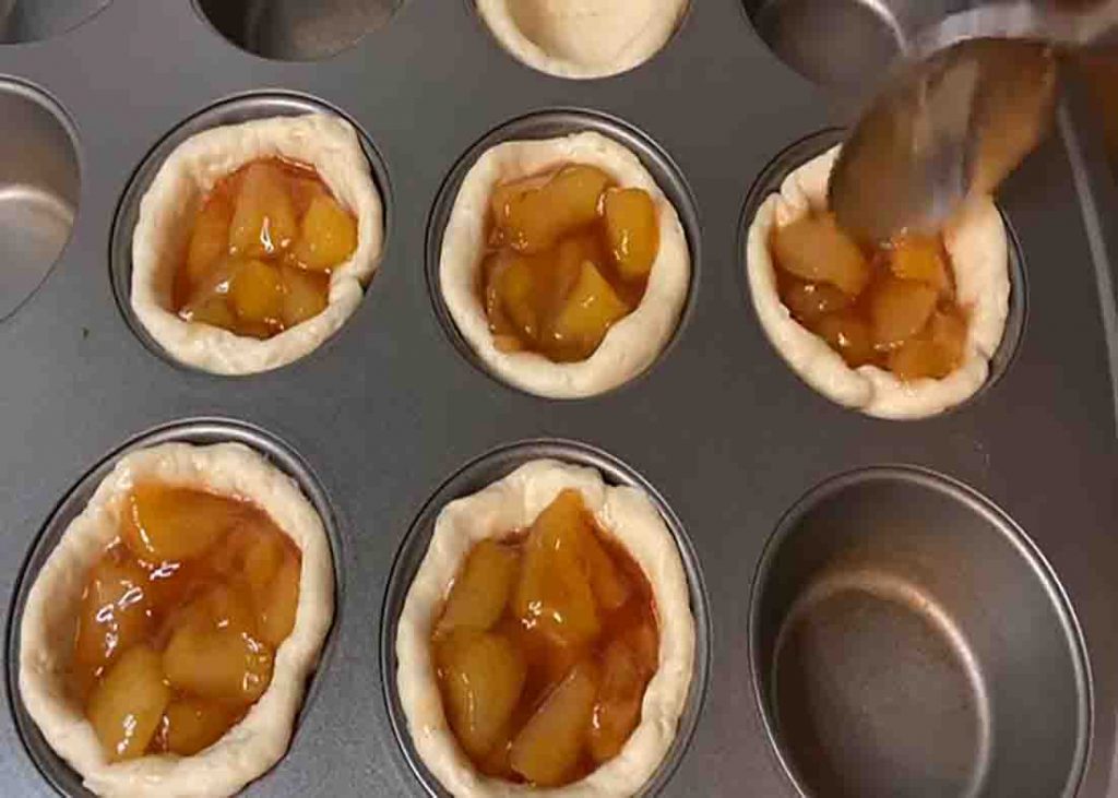 Dividing the apple mixture on each biscuit cups