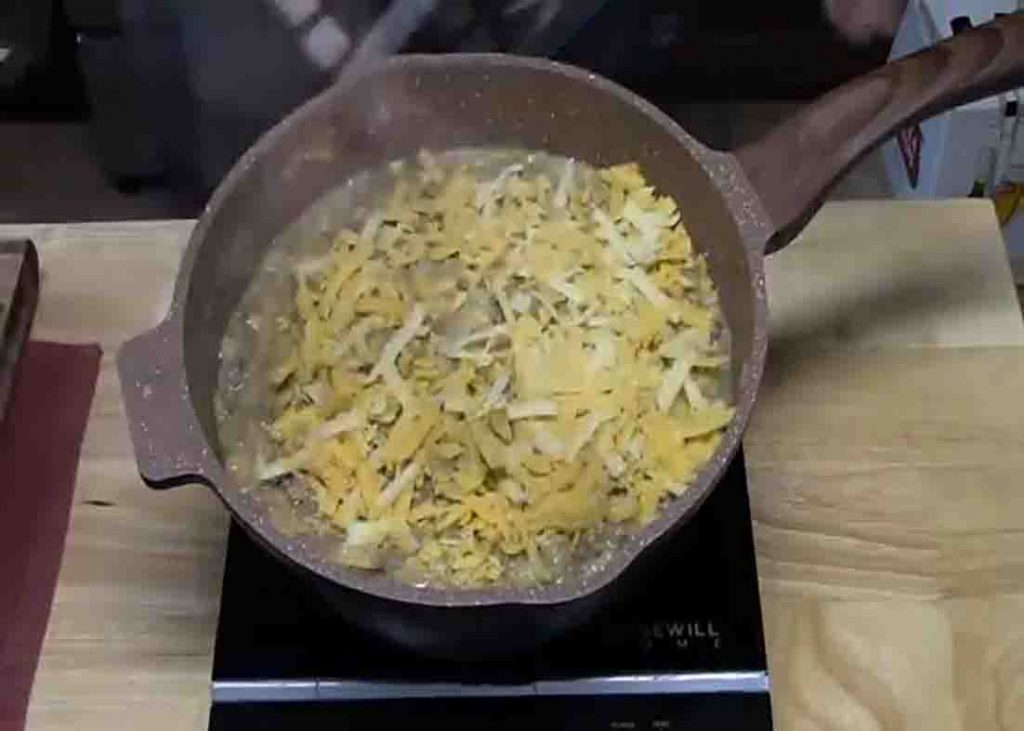 Adding shredded cheese to the potatoes and ground beef recipe