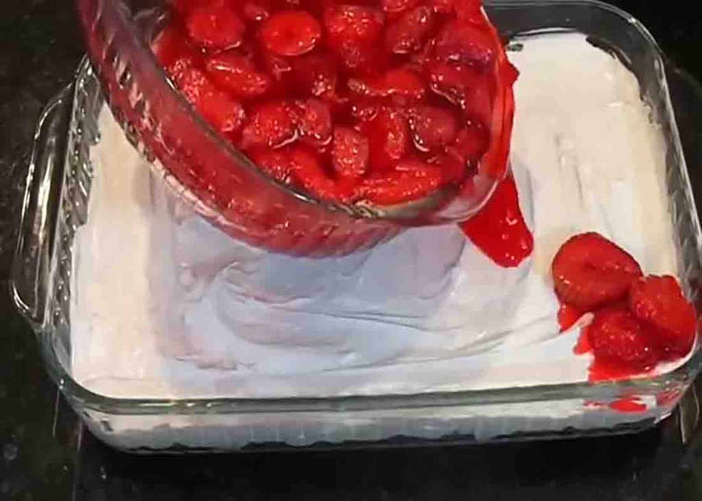 Pouring the strawberries on top of the pretzel and cool whip