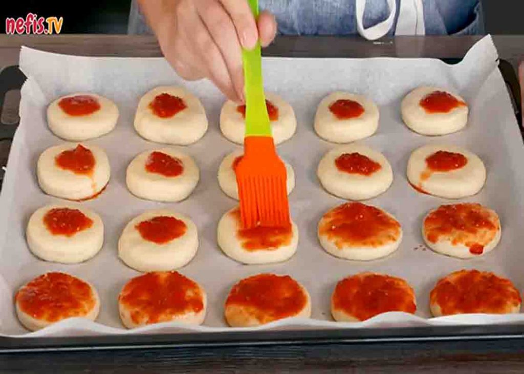 Spreading the pizza sauce on top of the pizza bites