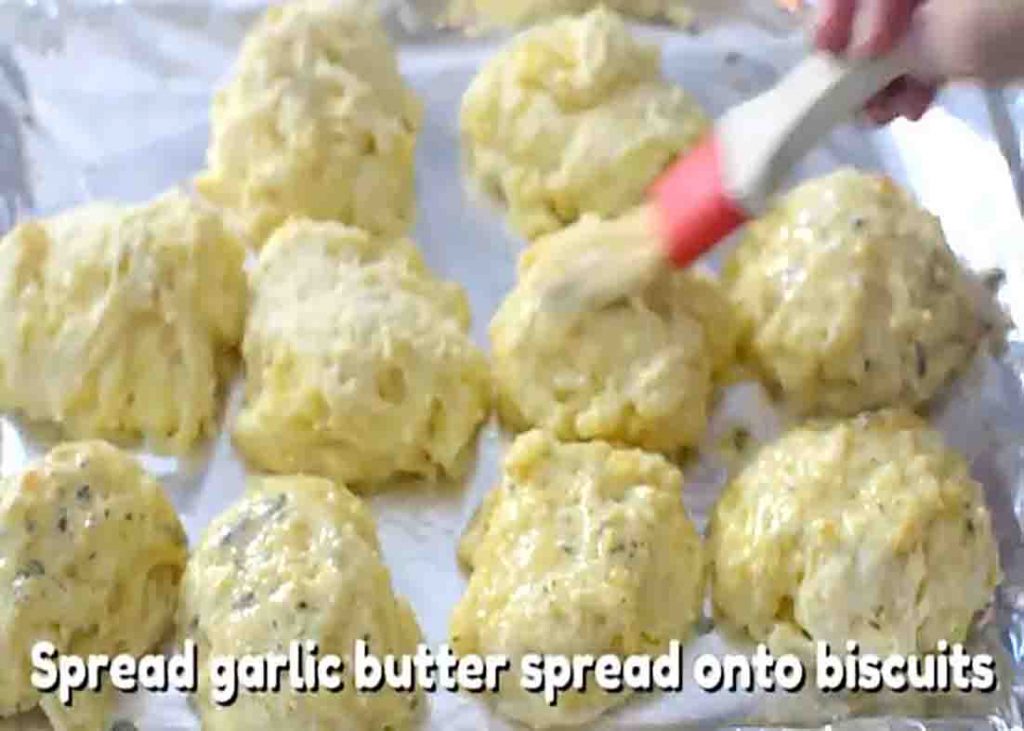 Spreading the garlic butter sauce over the cheddar bay biscuits