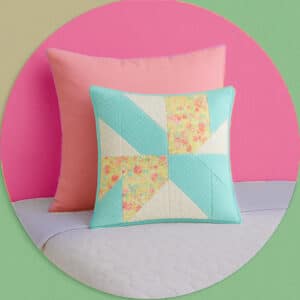 Handmade pillows and a quilted comforter in pastel colors arranged on a neatly made bed.
