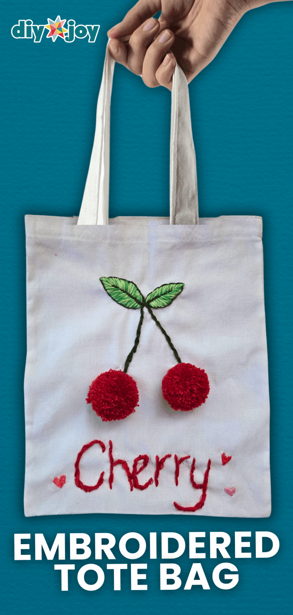 Embroidered Pom Pom Cherry Tote Bag White canvas tote bag with embroidered green leaves, two red yarn pom pom cherries and the word Cherry stitched in red