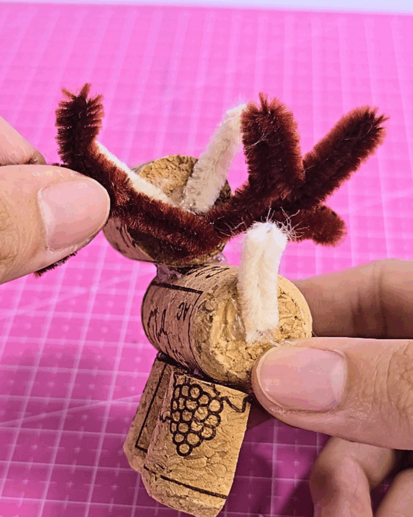 Holiday Crafts - hands attaching brown and white pipe cleaner antlers to a wine cork head
