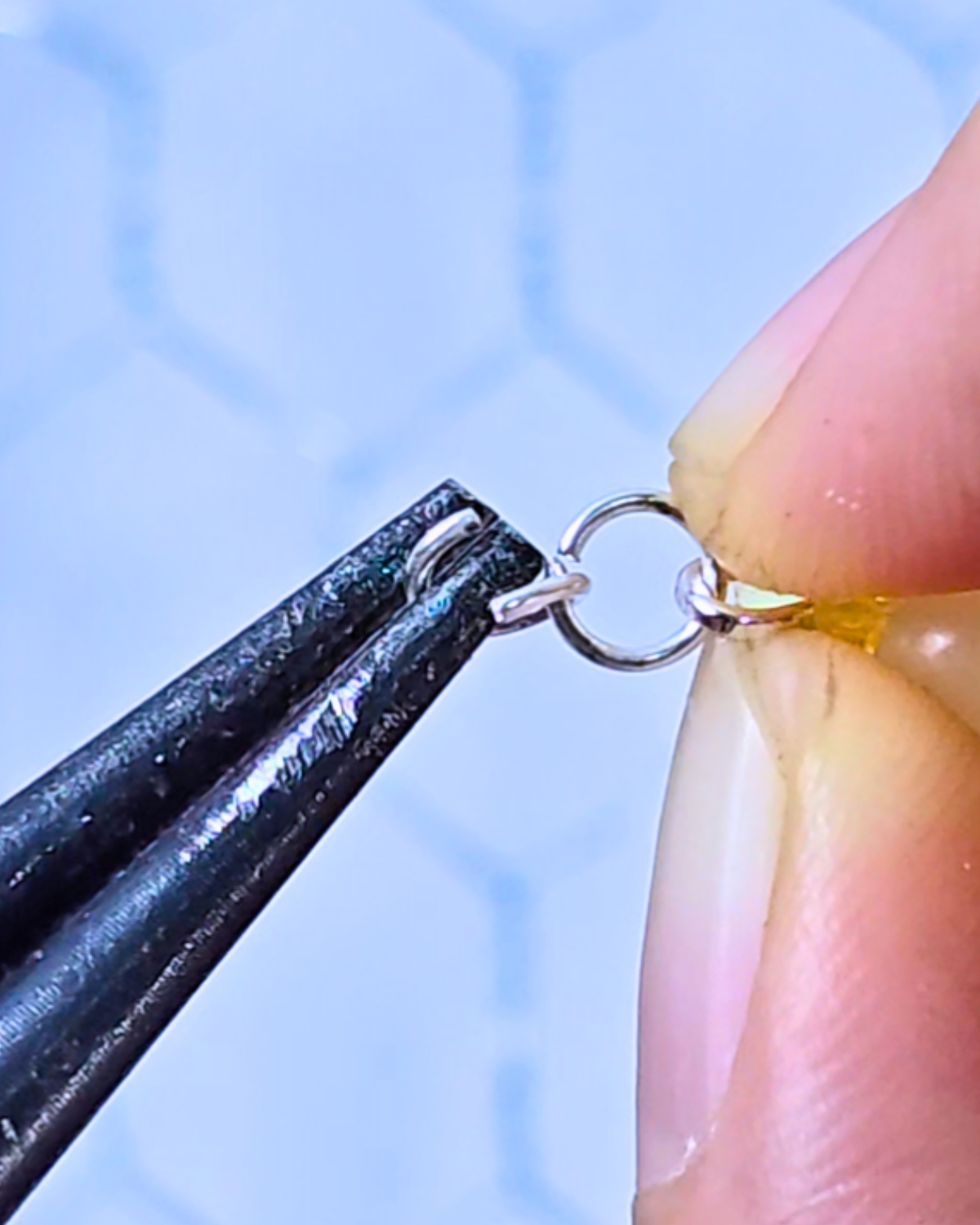 Close-up of pliers attaching a jump ring to a bead, showing how to prepare pieces for a picture frame suncatcher.