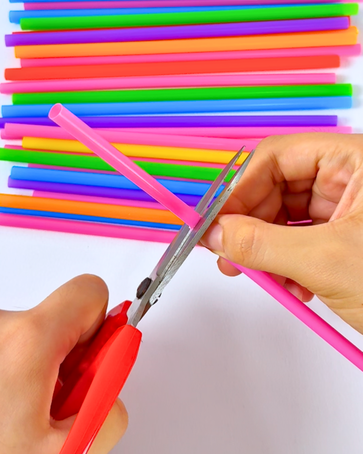 Cutting a pink cocktail straw in the middle to prepare the petals for the flower assembly.