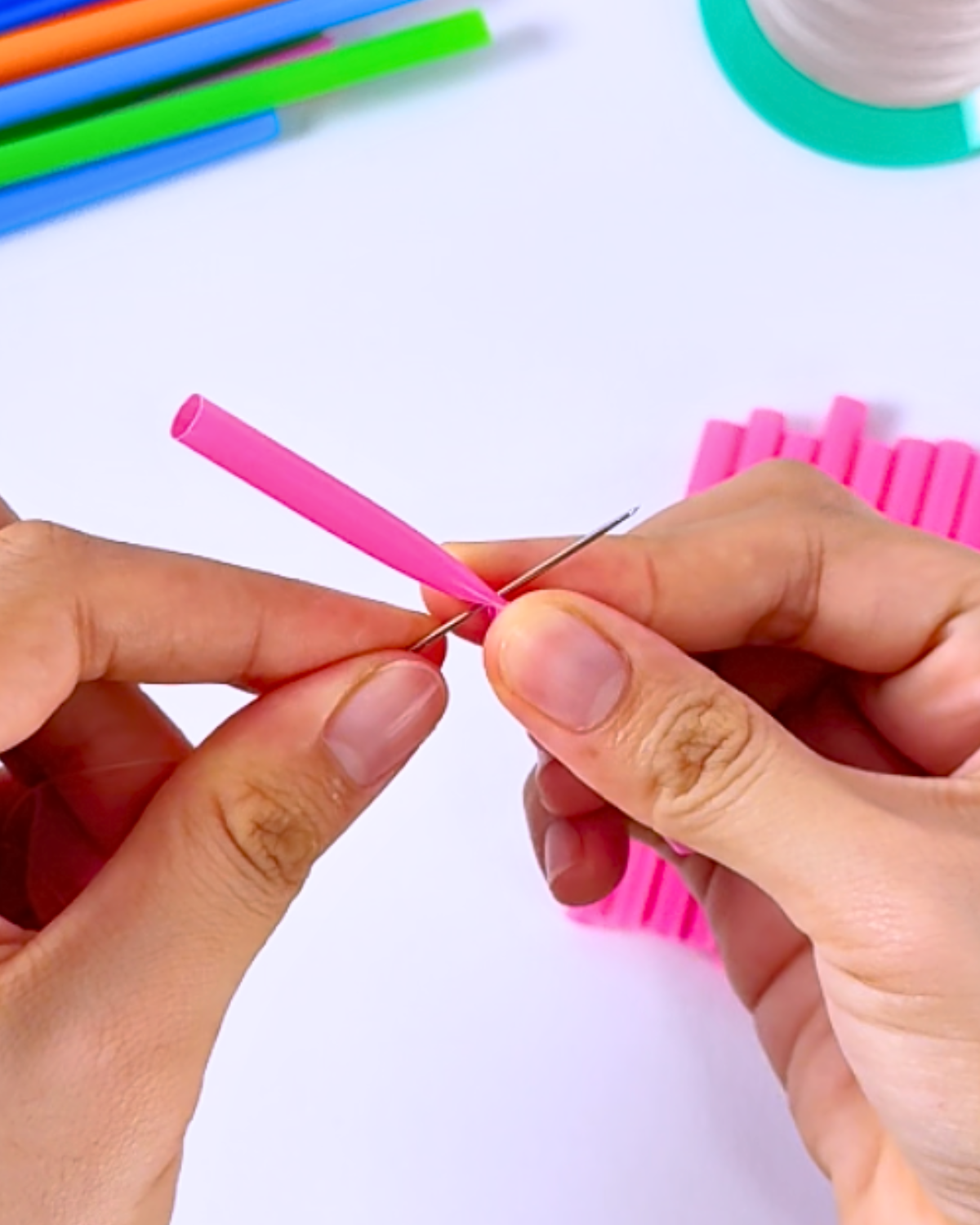 Inserting a needle into the center of a cut straw to assemble the cocktail straw flower parts together.