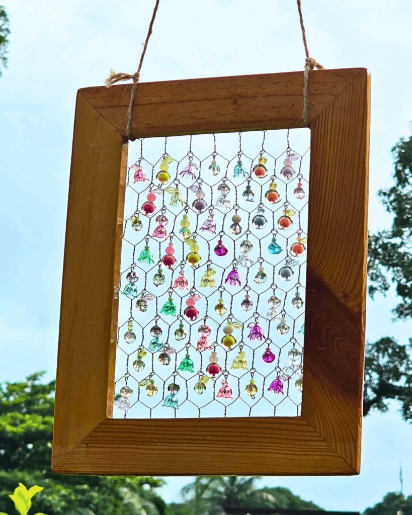 Hanging a picture frame suncatcher with beads on a tree branch outdoors.