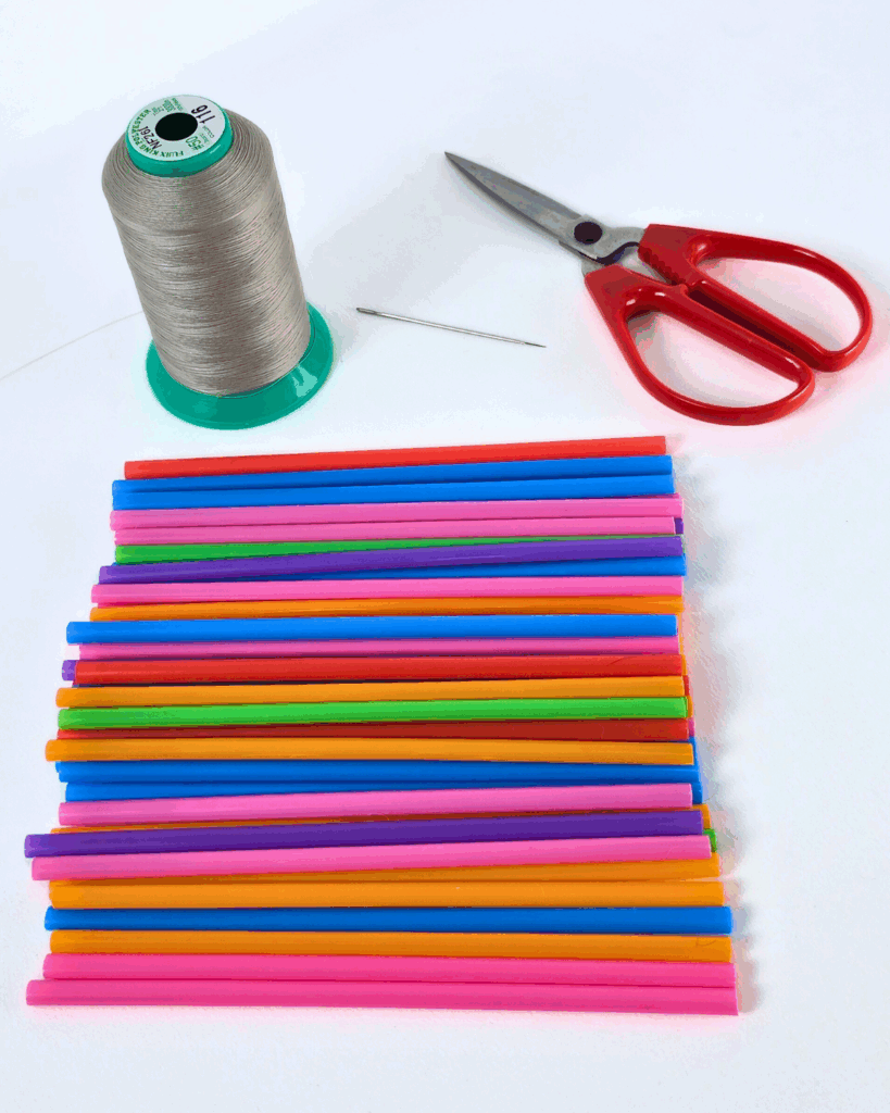 All needed materials for cocktail straw flowers, including straws, needle, thread, and scissors, arranged for crafting.