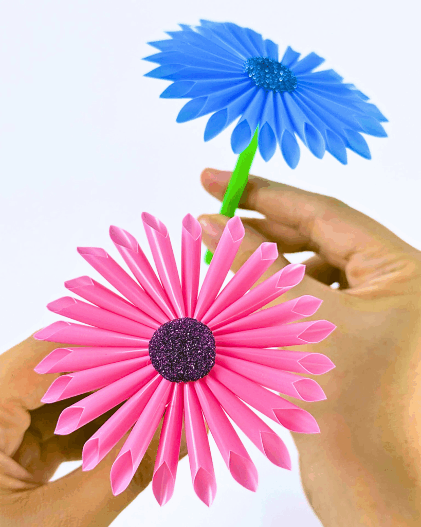 Hands holding two finished cocktail straw flowers to show the final result of the step-by-step craft.