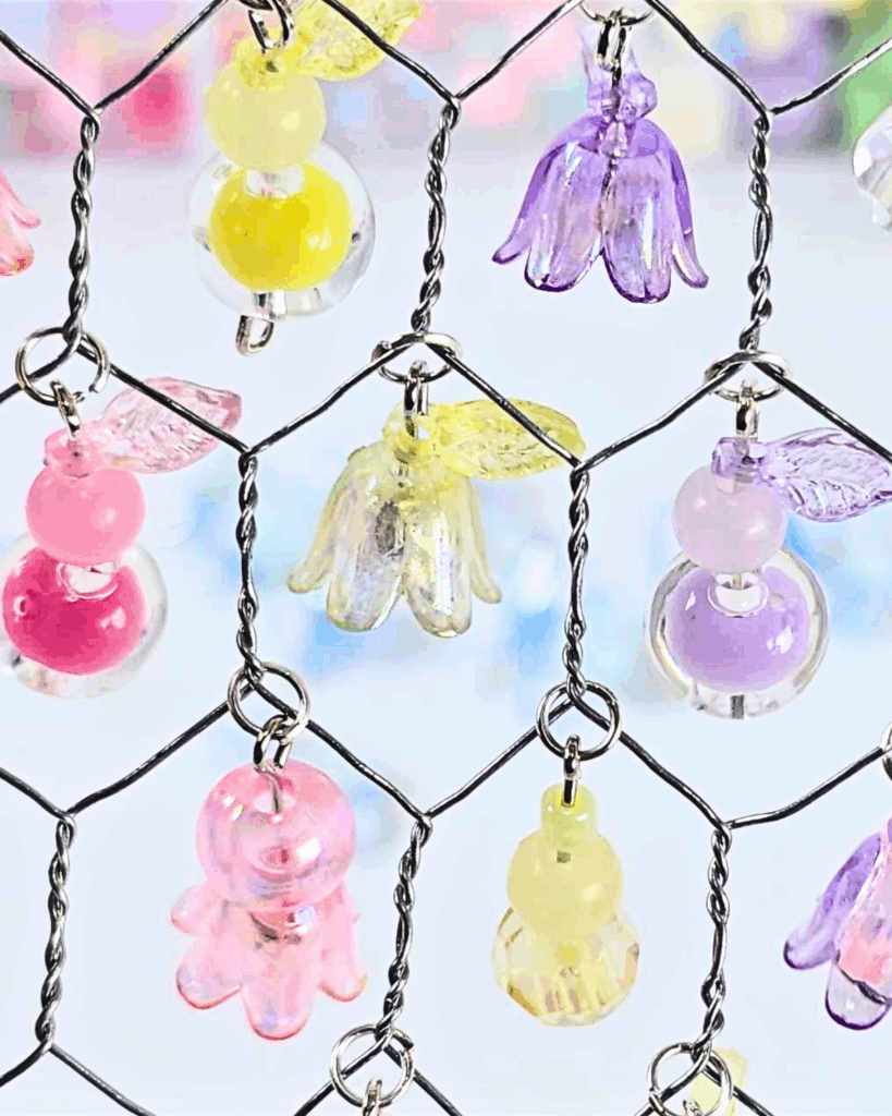 Close-up picture of colorful beads hanging on chicken wire inside a picture frame.