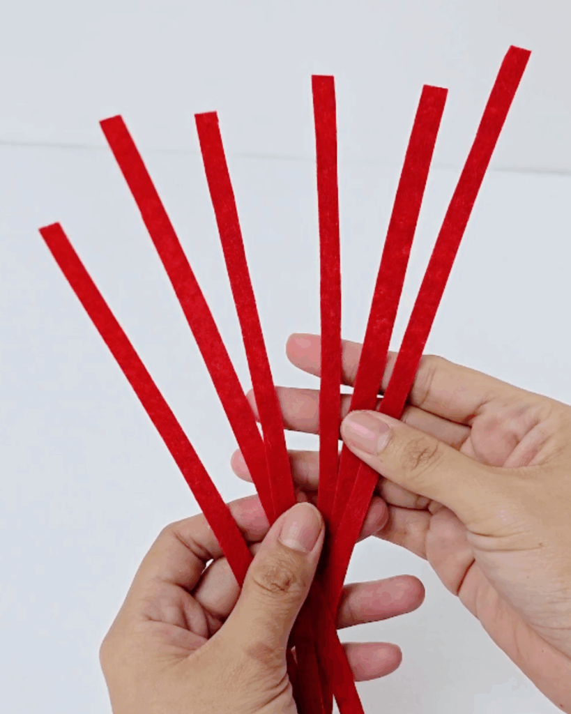 DIY Halloween Props - two hands holding a fan of six thin red strips of varying lengths against a white background, cut ready to wrap the lollipop stick