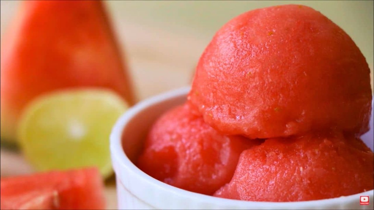 Three Ingredient Watermelon Sorbet Scoops of bright red watermelon sorbet in a white bowl beside fresh watermelon wedges and a whole lemon