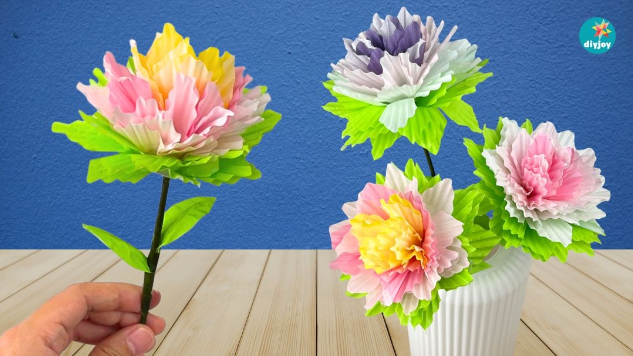 Paper flower bouquet using cupcake liners, pink and yellow ruffled paper blooms with green leaves on stems in a white vase