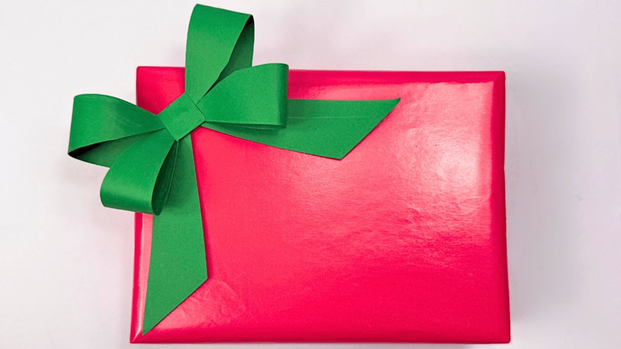 How to make a paper bow, a bright green folded paper bow with long tails glued to the corner of a hot pink wrapped gift