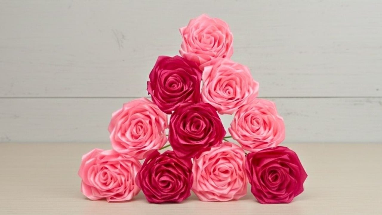 Satin ribbon roses in pale pink and deep magenta stacked into a neat pyramid on a pale wooden surface