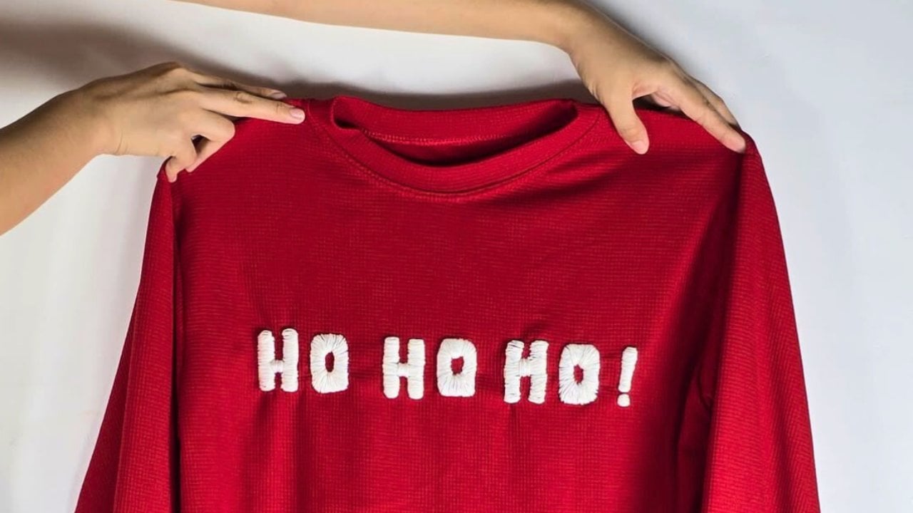 A red knit sweater reading HO HO HO in raised white embroidered letters worked over a hot glue outline