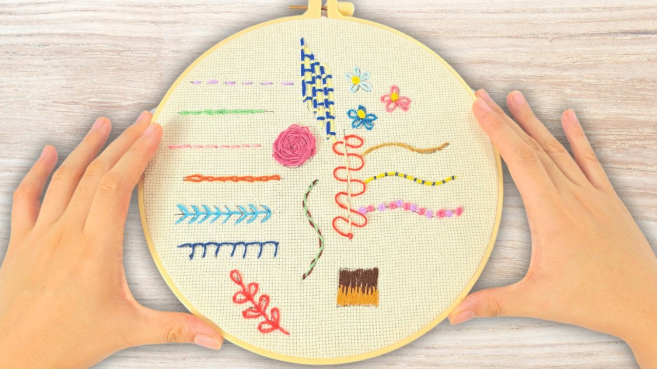 An embroidery hoop holding fabric worked with fifteen basic hand embroidery stitches in colored thread