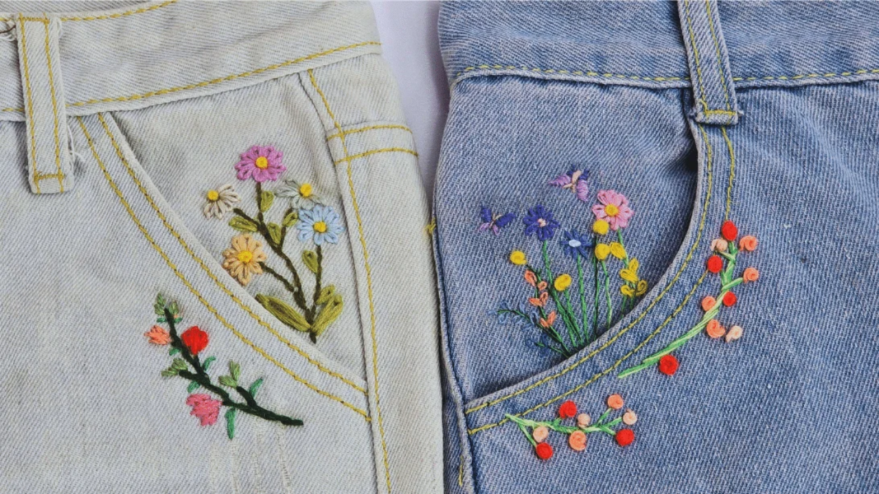 Two pairs of jeans, one pale and one blue, with flowers embroidered around the pockets in pink, yellow and red